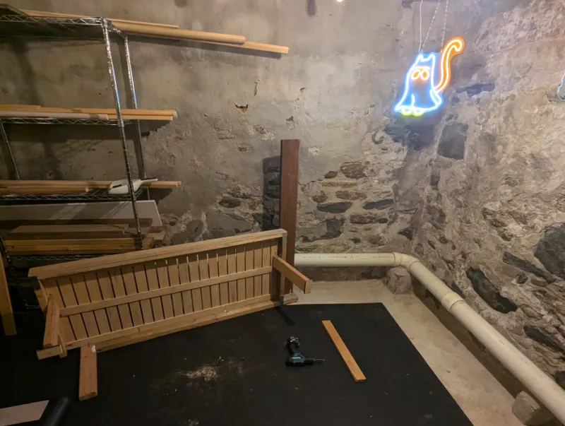 Partially assembled wooden daybed frame on its side under a neon cat sign
